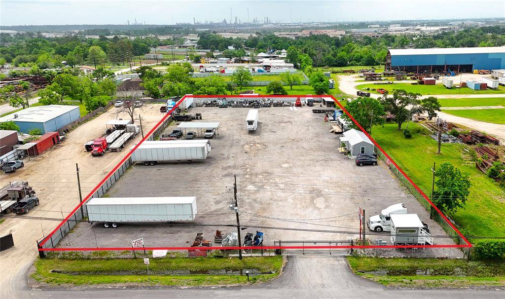 This photo shows a large, fenced industrial lot suitable for commercial use. The space is paved, accommodating trailers and equipment, with easy access from the road. It's surrounded by greenery and other industrial properties. Ideal for storage or logistics.