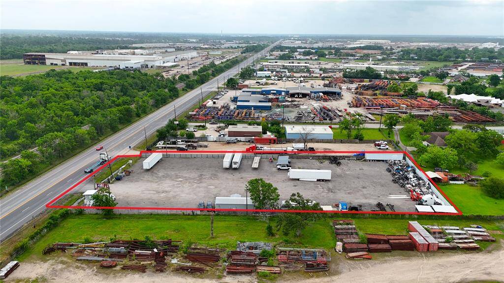 This aerial photo showcases a large industrial property outlined in red, featuring a spacious paved lot with several trucks and equipment. It's situated along a main road with other industrial and commercial facilities nearby, offering ample space for business operations.