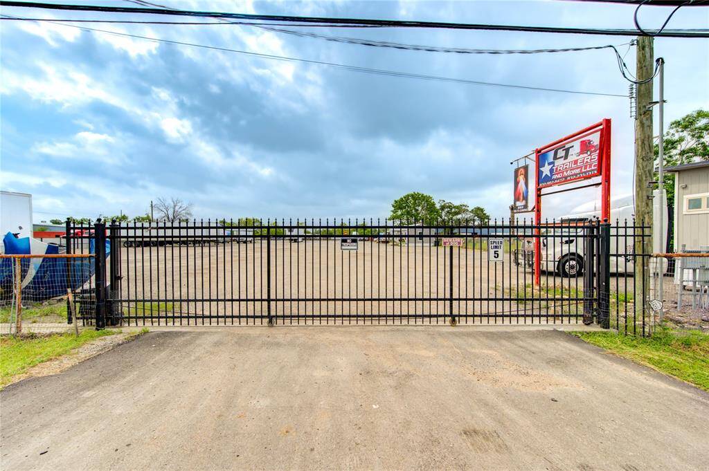 This photo shows a gated entrance to a large gravel lot, possibly used for storage or parking, with a commercial sign on the right. The area is fenced and surrounded by open space, offering security and accessibility.