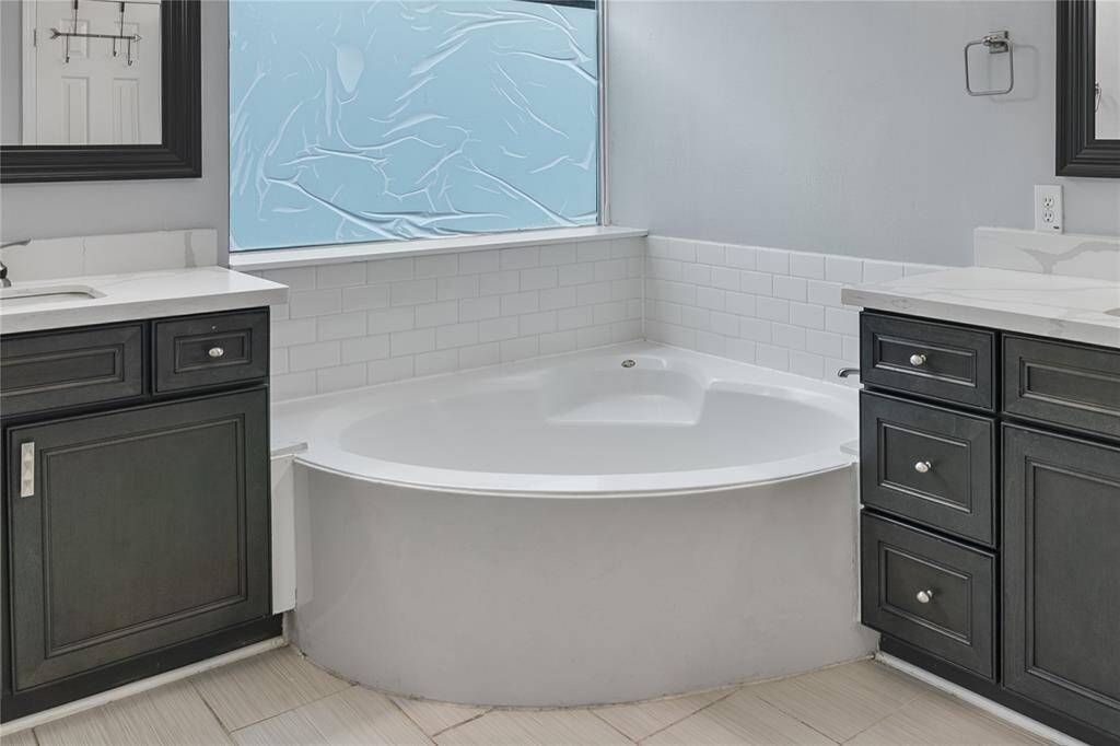 Luxurious spa-like bathroom featuring dual vanities with quartz countertops, elegant framed mirrors, a relaxing soaking tub under a dramatic arched ceiling, and sleek dark cabinetry for a bold, modern finish.