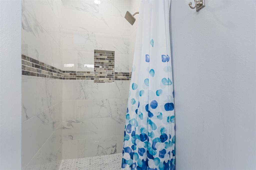 Modern walk-in shower with frameless glass, oversized marble-look tile, and an eye-catching mosaic accent band—perfectly paired with quartz counters and sleek cabinetry for a refined, spa-inspired retreat.