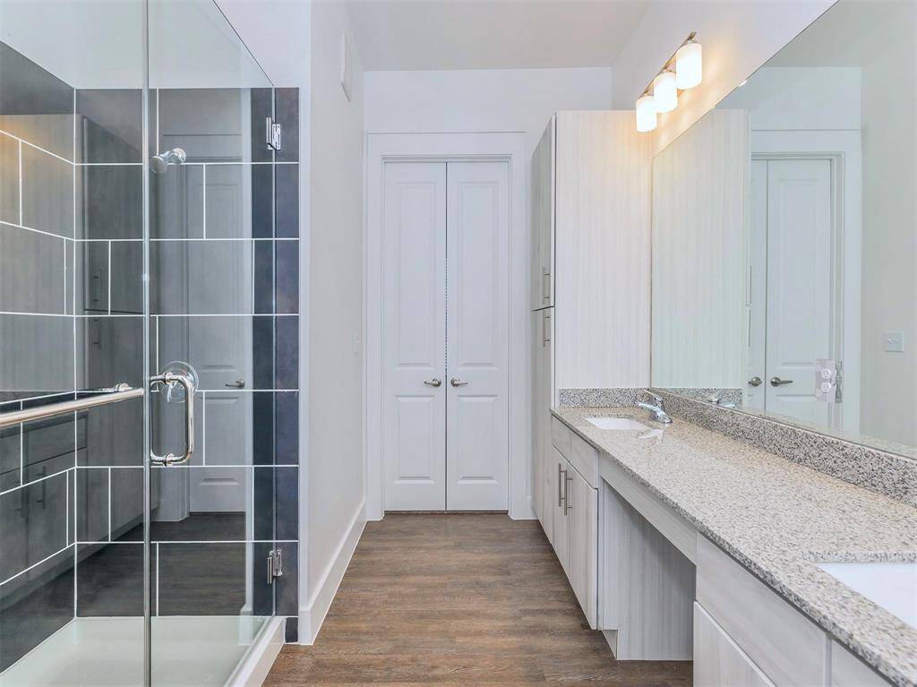 Spacious bathroom with double sinks, walk-in shower, modern finishes, and granite countertops