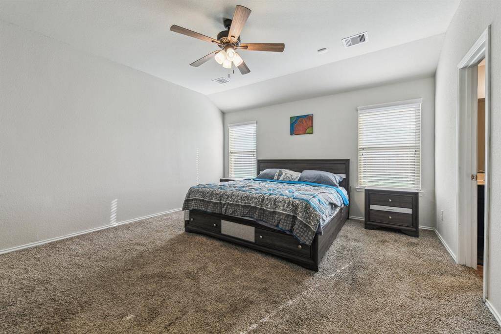 This spacious bedroom features neutral walls, carpeting, and a ceiling fan. The two windows provides natural light, and an en-suite bathroom for convenience.