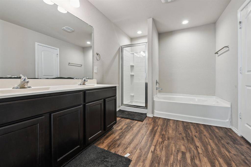 This modern bathroom features a double sink vanity with dark cabinetry, a spacious walk-in shower, and a separate bathtub. It has sleek wood-look flooring and neutral-colored walls, creating a clean and inviting space.