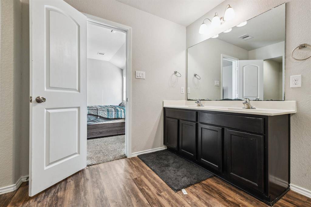 It features a large mirror and wood-look flooring, with an open door leading to a bedroom.