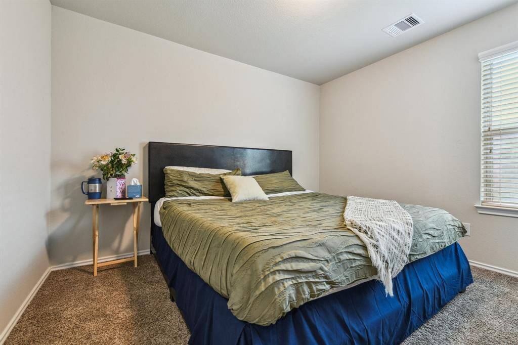 This cozy bedroom features neutral walls and soft carpeting. Natural light fills the space through a window, creating a warm and inviting atmosphere.
