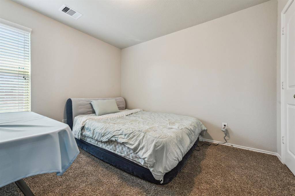 Cozy bedroom with neutral walls and carpet, featuring a window with blinds for natural light. Simple and functional space, ideal for relaxation.