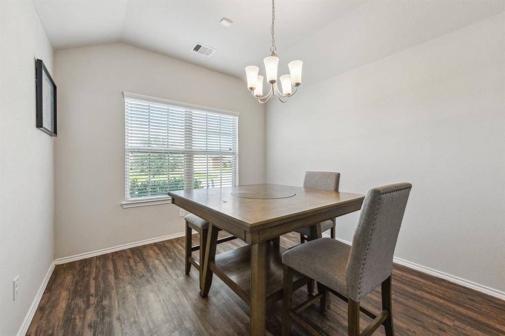 This photo showcases a bright dining room with a wooden floor, neutral walls, and a ceiling light fixture. It features a wooden table with two upholstered chairs, and a large window providing natural light.