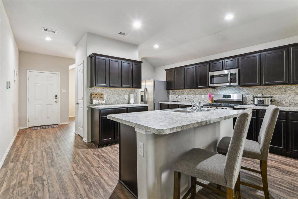 This photo showcases a modern kitchen with dark cabinetry, stainless steel appliances, and a spacious island with seating. The open layout and wood flooring create a warm, inviting atmosphere.