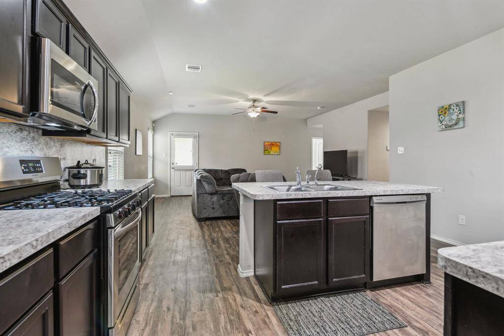 The kitchen island includes a sink and dishwasher, leading into a cozy living space with a ceiling fan and natural light.