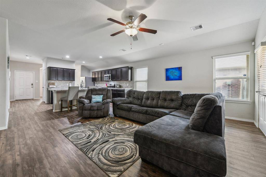 Natural light streams through multiple windows, highlighting the wood-style flooring and ceiling fan.