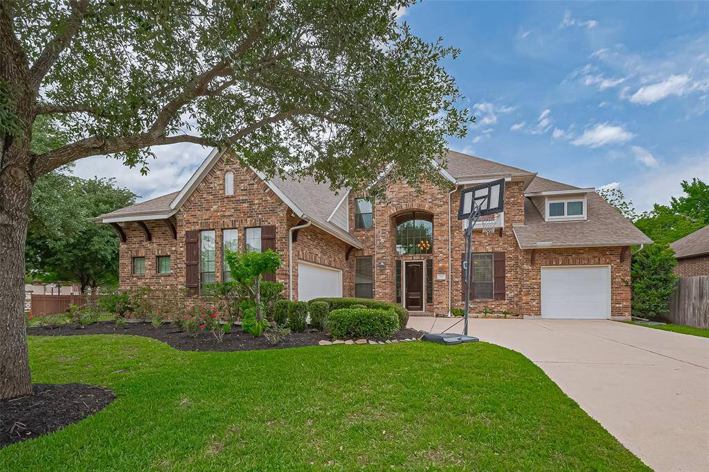 This charming brick home features a well-maintained front yard with mature trees and landscaping. It includes a three-car garage and inviting large windows.