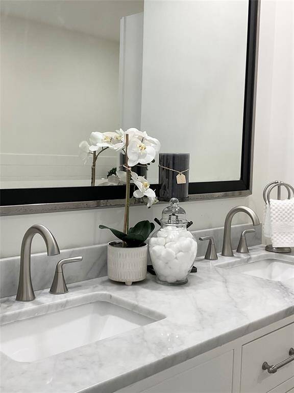 This is a modern bathroom with a sleek marble countertop, an elegant silver faucet, and a large mirror. A vase with white flowers adds a touch of sophistication and freshness.