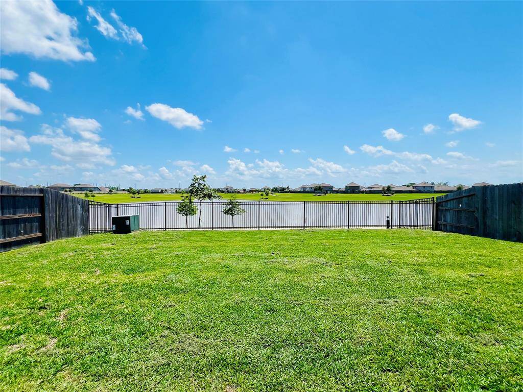 Spacious backyard with a lush green lawn, fenced for privacy, and offering picturesque views of a serene lake under a clear blue sky. Ideal for relaxation and outdoor activities.