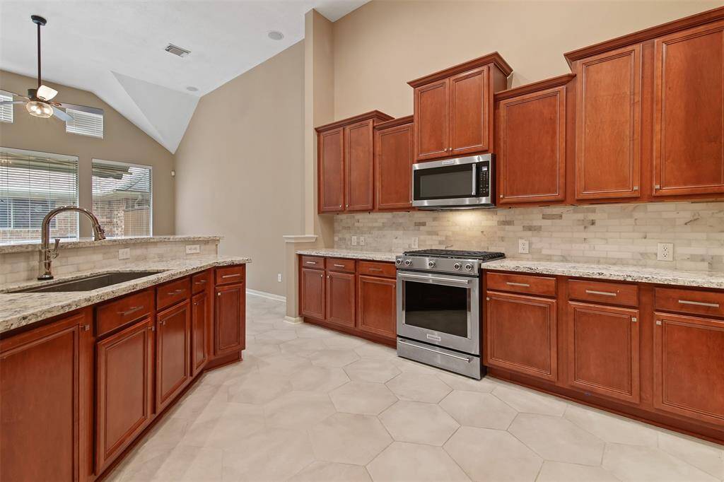 Another view of the kitchen with granite countertops, decorative tile backsplash, under cabinet lighting, undermount single basin sink and ss gas range.
