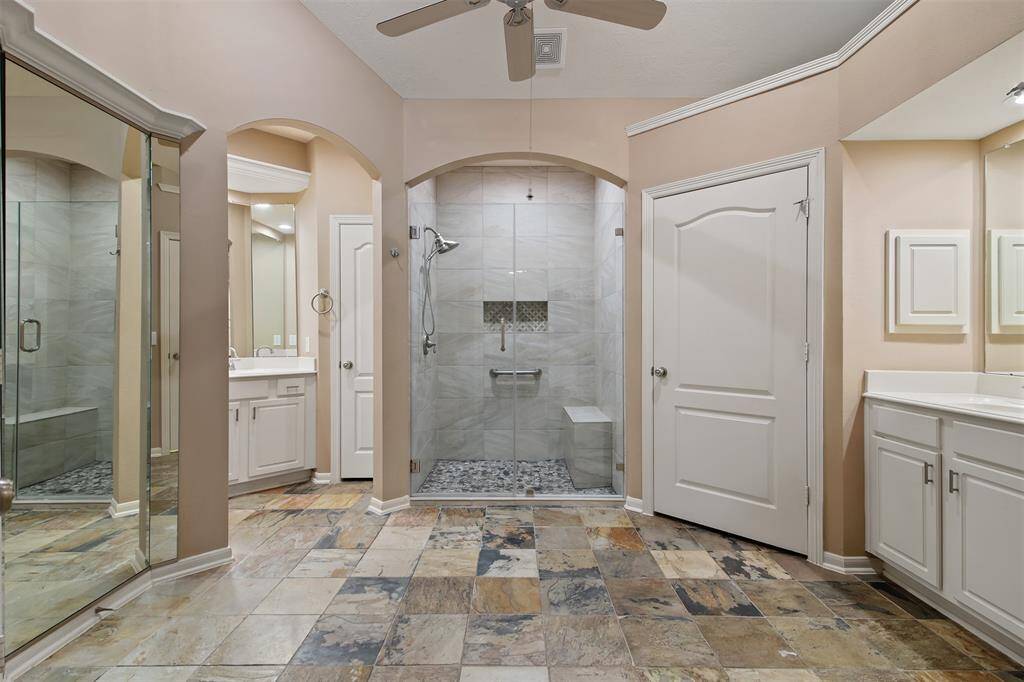 Spa like primary bathroom features slate floors, double vanities and ceiling fan.