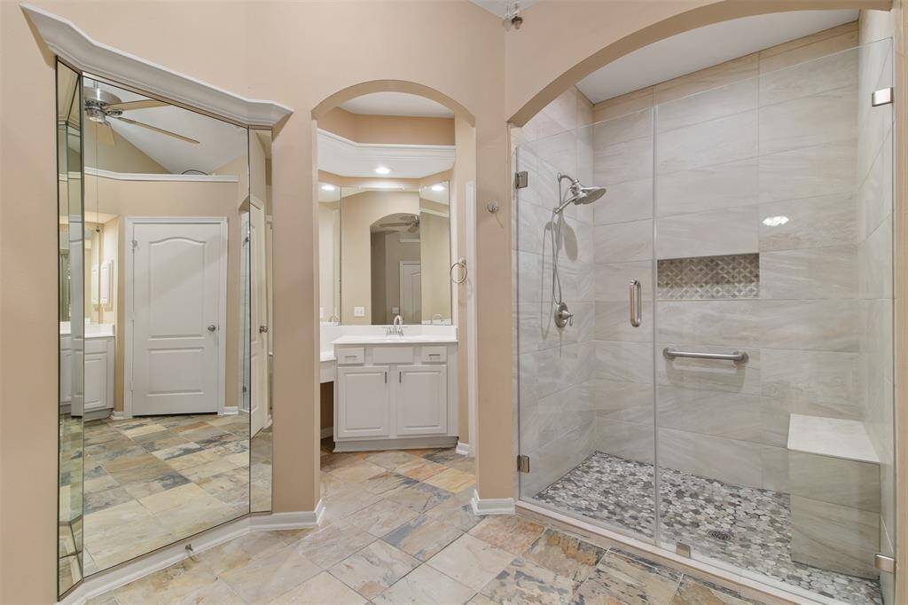 Updated walk in glass shower with pebble flooring and bench seat. Primary bathroom also features a built in full length mirror.