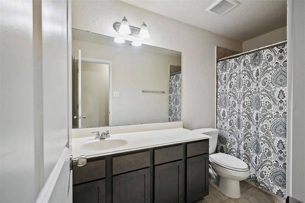 This bathroom features a clean, modern design with a large mirror, vanity lighting, a dark wood vanity with ample storage, and a shower-tub combo.