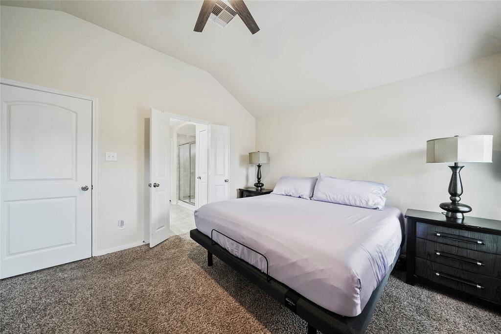 This primary bedroom features a cozy carpet, vaulted ceiling, and ample natural light.