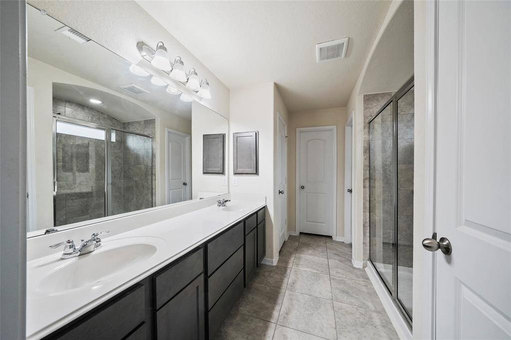 This modern bathroom features a double vanity with sleek dark cabinets and a large mirror. It includes a spacious glass-enclosed walk-in shower and is well-lit with contemporary fixtures. The neutral tile flooring adds a clean, elegant touch.