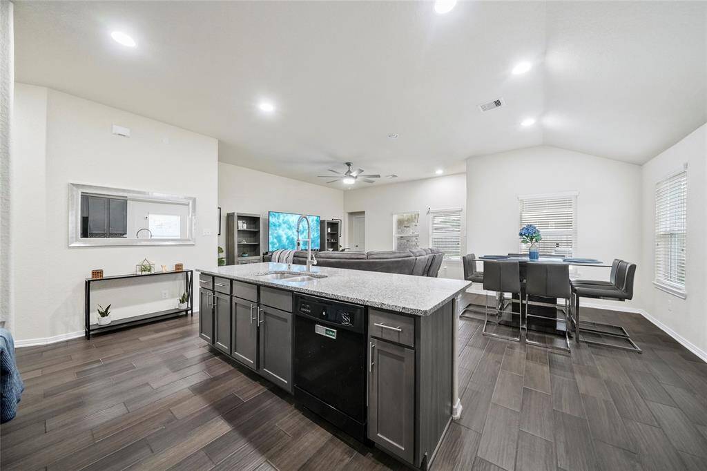 This photo showcases an open-concept living area with a modern kitchen featuring a large island, granite countertops, and beautiful cabinetry. The space includes a dining area and a cozy living room with ample natural light and neutral décor.