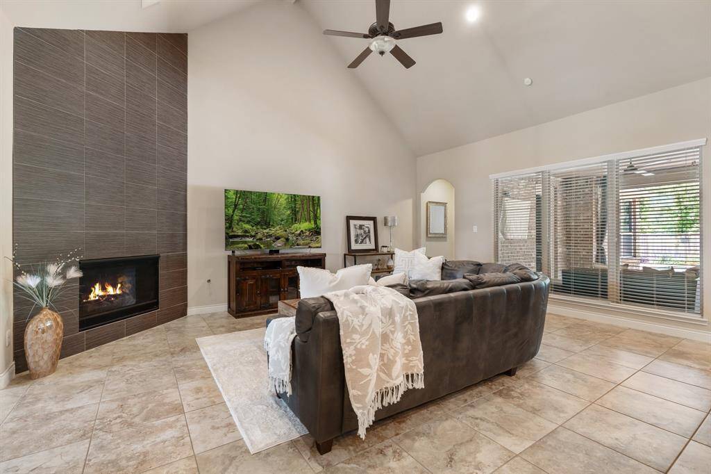 Family room with cathedral ceilings, tile flooring, and a beautiful modern accent wall with gas log inset fireplace.  Plenty of windows with natural light overlooking one of the covered porches, and the beautiful backyard.