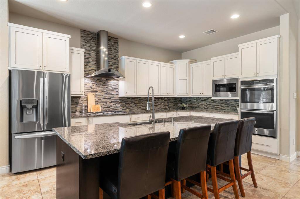 Modern kitchen with upgraded stainless steel appliances, white cabinets, sleek stainless steel range hood, huge kitchen island with wood finish, and granite countertops. There are drawers below the stainless steel gas range for storing your pots and pans!