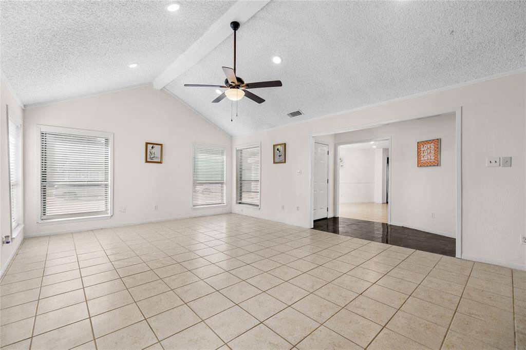 This is a spacious living area featuring a vaulted ceiling with a ceiling fan, tile flooring, a cozy fireplace, and ample natural light from the windows with new 2" blinds.There's also built-in shelving for extra storage or display.