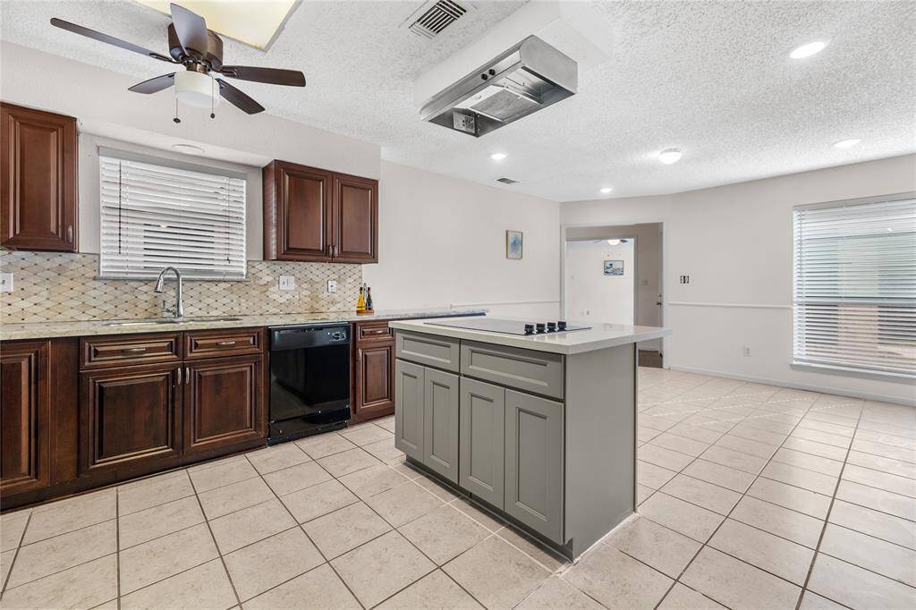 Kitchen features recent dark wood cabinets with handles, high end granite countertops, a decorative tile backsplash, and stainless steel and black appliances, complete with a ceiling fan and tile flooring.