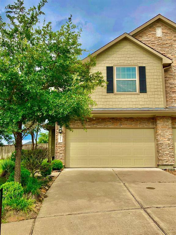 A charming two-story home with a stone and siding exterior, featuring a two-car garage and a neat front yard with a tree and shrubs.