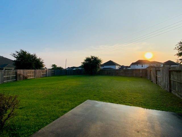 A spacious backyard with a well-maintained lawn, surrounded by a wooden fence. The open area is perfect for outdoor activities, and the sunset view adds a serene touch to the space.