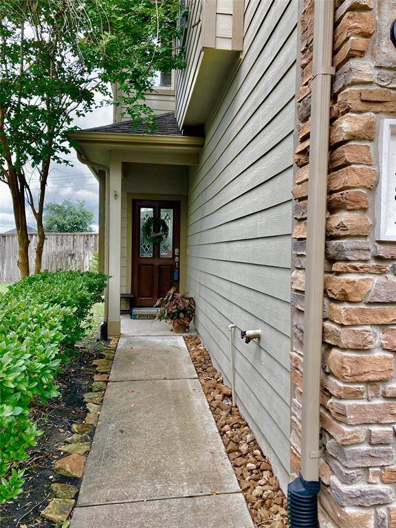 Charming entryway with a stone-accented facade and a well-maintained pathway. Lush greenery lines the path leading to a welcoming wooden front door, creating a cozy and inviting first impression.
