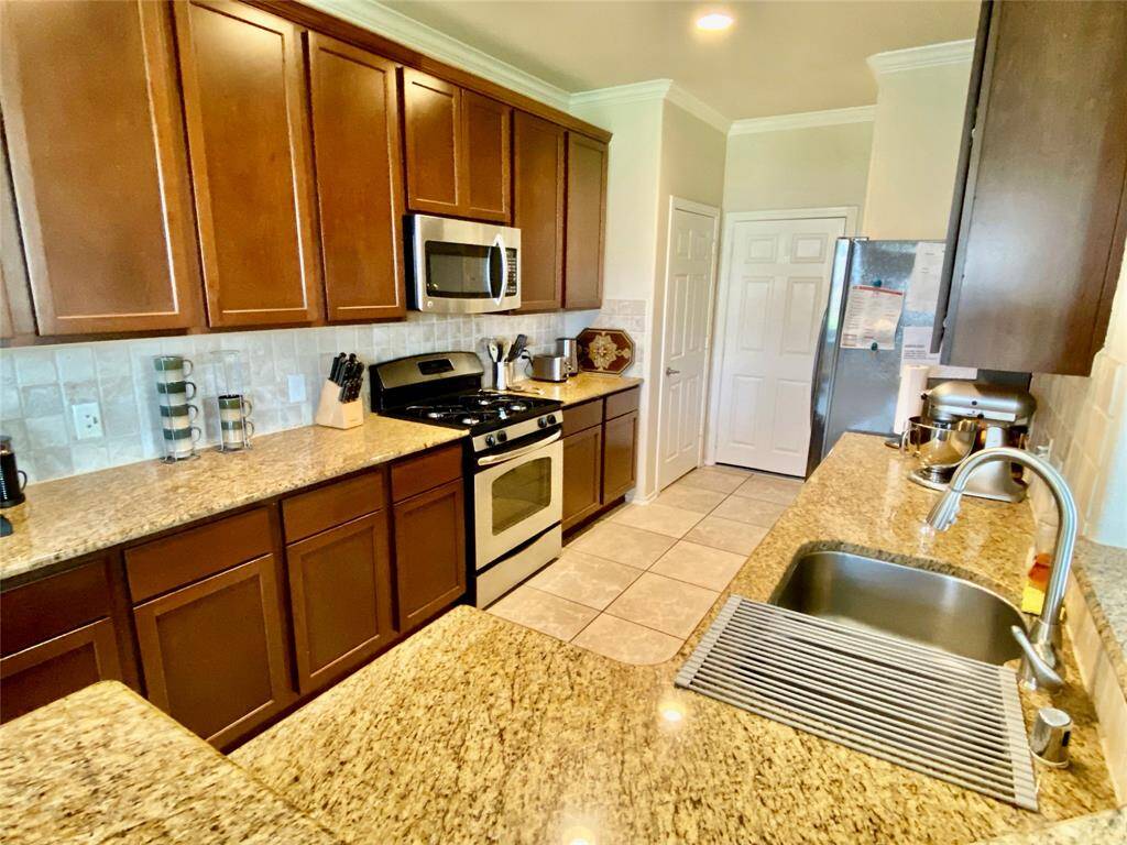 This kitchen features elegant wooden cabinetry and granite countertops, complemented by stainless steel appliances. The space is well-lit with recessed lighting and includes a double sink and ample storage. Tile flooring adds a clean, durable finish.