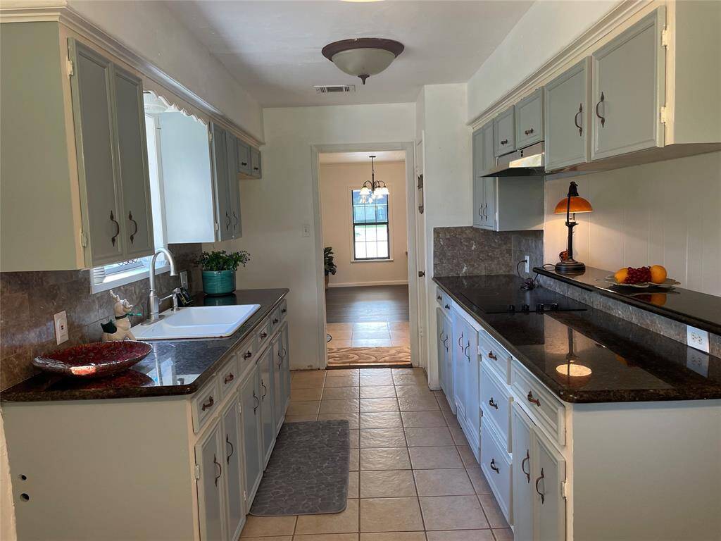 Neat kitchen next to dining area, offers granite countertops, double sinks, electric  cooktop, and a lot of storage space.