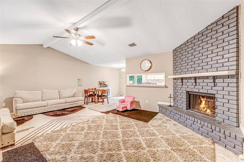 Cozy and inviting living room with a vaulted ceiling, brick fireplace, and ample natural light, perfect for relaxing or entertaining.