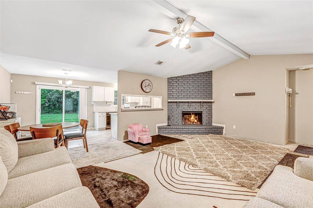 Spacious living room with a cozy fireplace, vaulted ceiling, and natural light flowing from the adjacent dining area. Perfect for gatherings and relaxation.