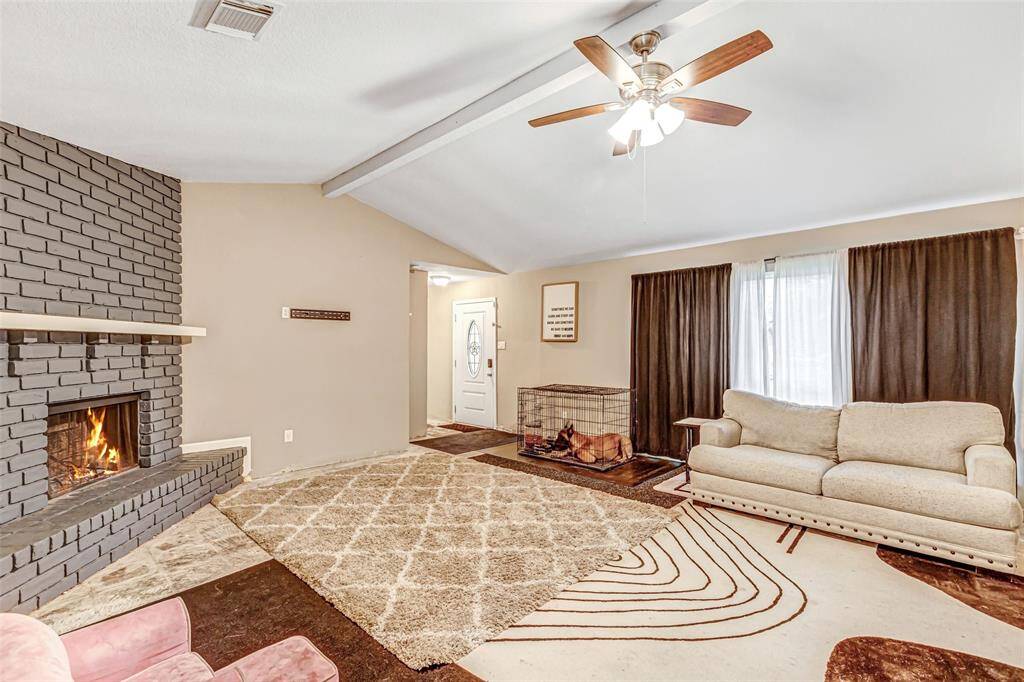 Cozy living room featuring a stylish brick fireplace, vaulted ceiling with fan, and abundant natural light. Perfect for relaxation and entertaining.