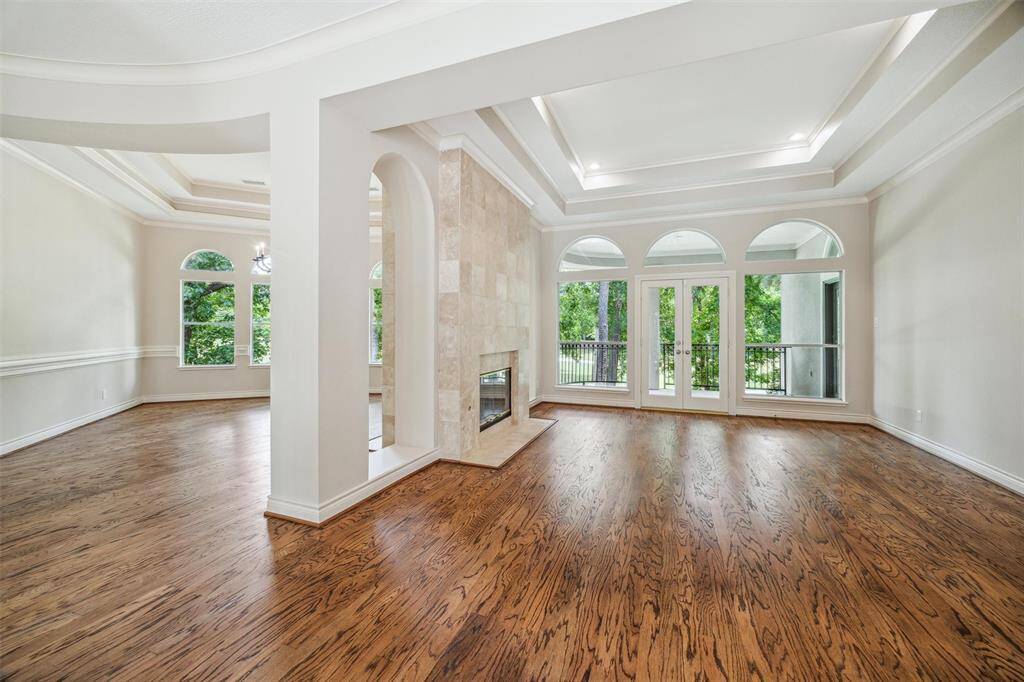 Spacious living area features elegant hardwood floors, large windows for abundant natural light, and a double-sided fireplace. The high tray ceilings add a touch of sophistication, while French doors open to a balcony that provides scenic outdoor views.