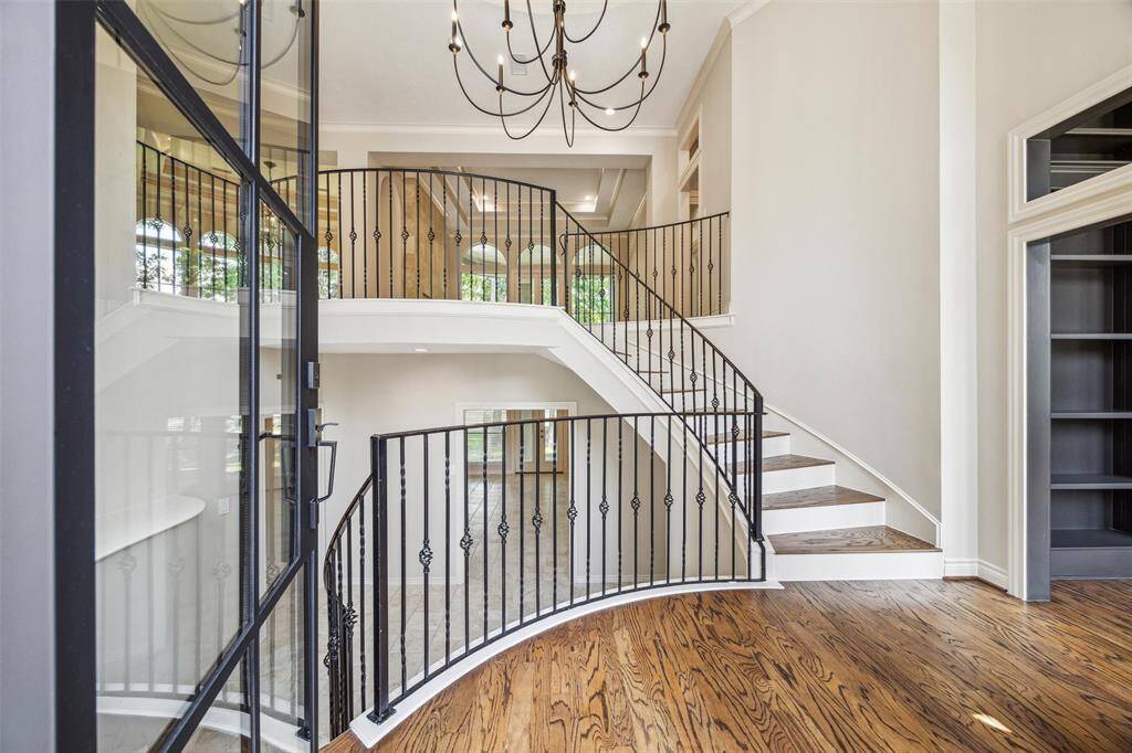 This elegant entryway features a grand staircase with wrought iron railings, a high ceiling with a stylish chandelier, and polished hardwood floors, creating a welcoming and sophisticated atmosphere.