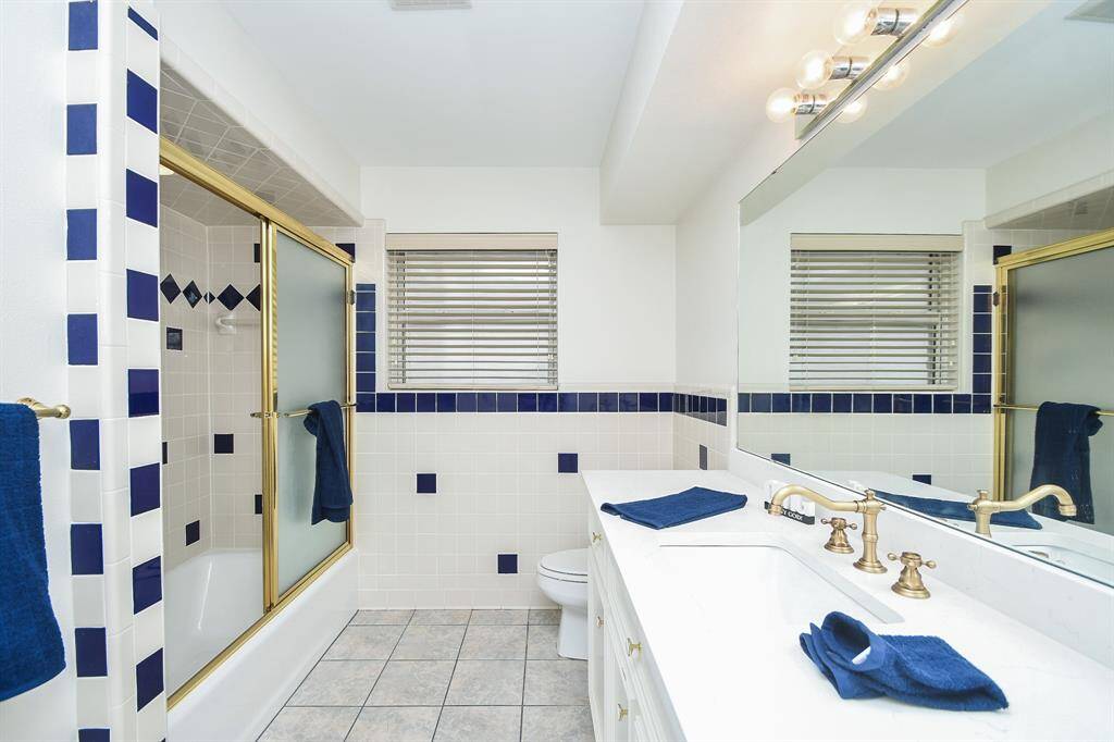 Happy tile detail makes this primary ensuite bath a sought after location; with shining wall-wide mirror and Hollywood lighting above sink and cabinetry. and combined shower/bathtub just opposite a roomy path.