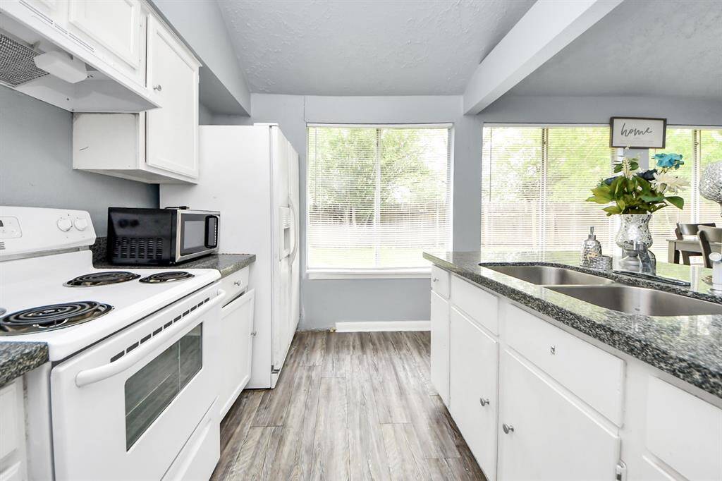Bright kitchen with modern finishes, featuring white cabinetry, granite countertops, and stainless steel double sink. Large windows offer plenty of natural light, complementing the spacious, open layout with room for dining.