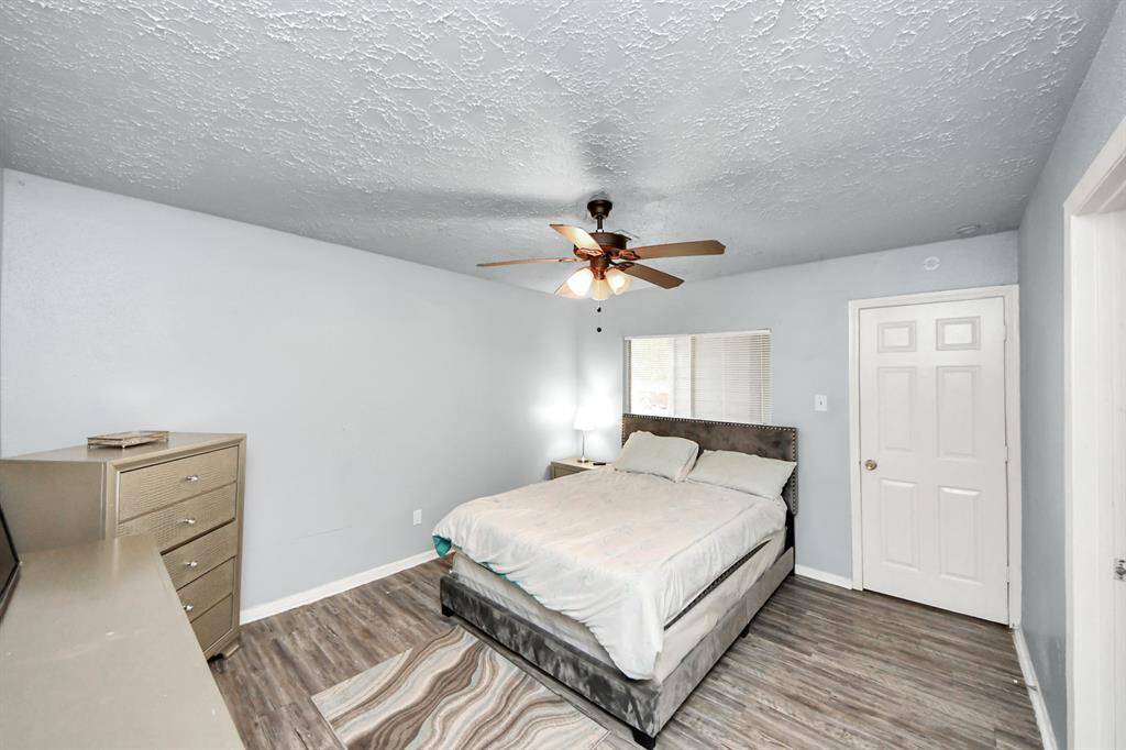 This primary bedroom features a modern design with light gray walls, ceiling fan and wood-style flooring. Plenty of space for bedroom furniture.