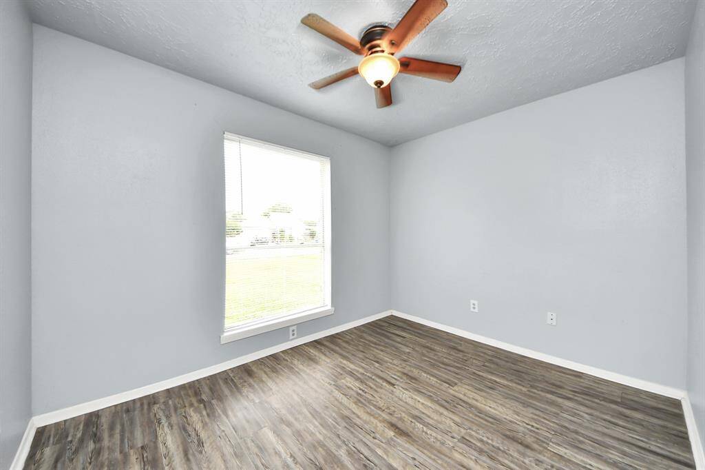 The third bedroom features light gray walls, wood-style flooring, and a ceiling fan with a light. It has a large window that allows natural light to fill the space, creating a bright and inviting atmosphere. Perfect for a home office our guest bedroom