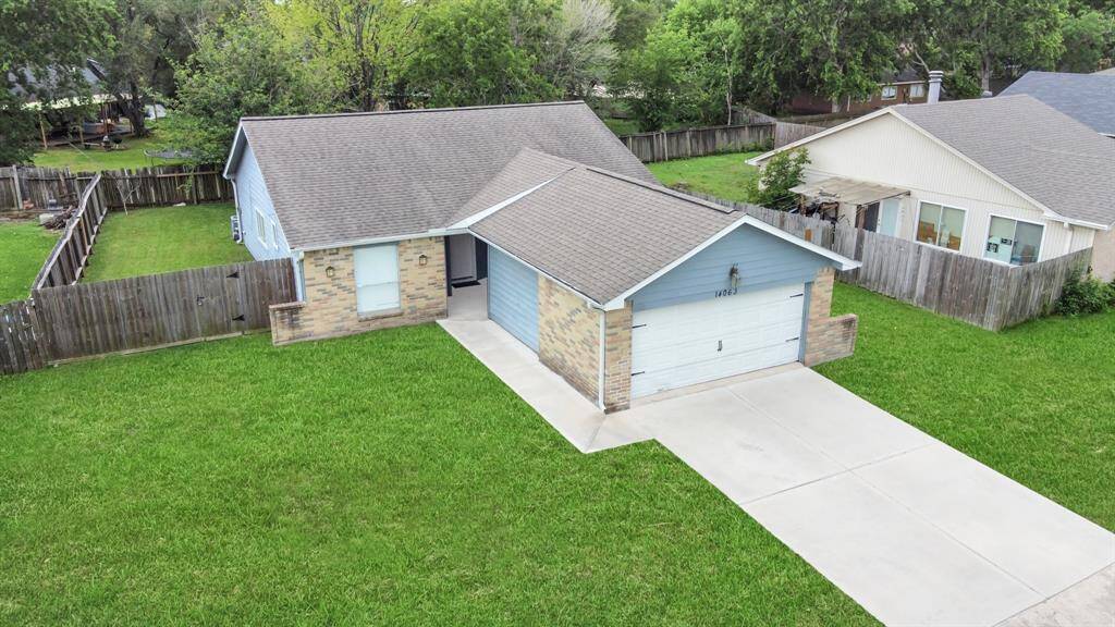 Charming single-story home with a spacious front yard and a long driveway leading to a two-car garage. The exterior features a mix of brick and siding, and the property is enclosed by a wooden fence, offering privacy.