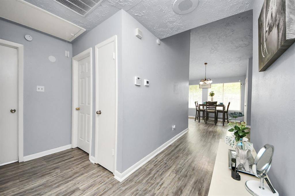 This photo showcases a modern, bright hallway with light gray walls, wood flooring, and a view into a dining area.