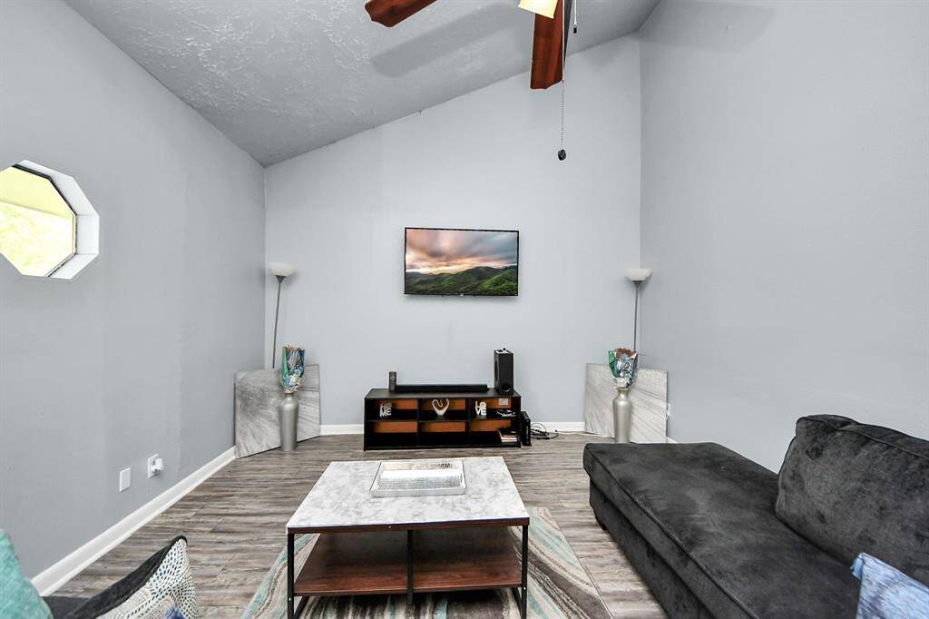 This living room features a high vaulted ceiling, modern gray walls, and wood-look flooring.