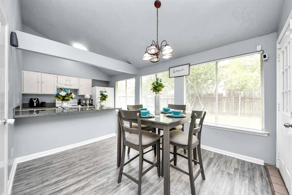 Bright dining area with large windows, modern gray flooring, and a cozy kitchen bar. Ideal for entertaining.