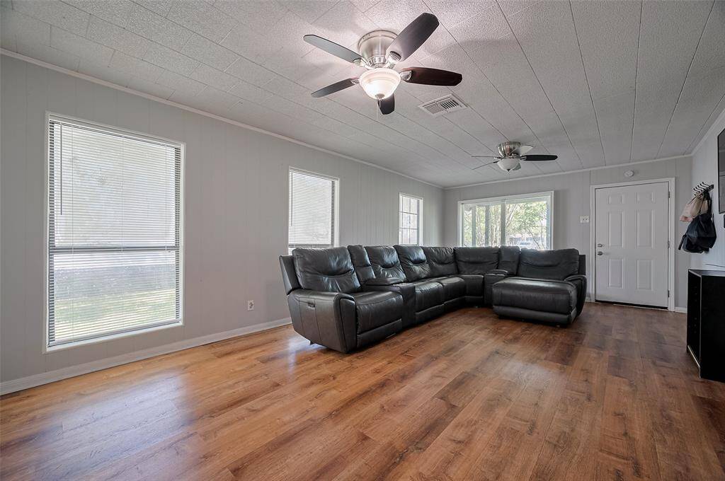 In the living area, oversized windows flood the room with natural light and two ceiling fans enhance comfort. Wood-style floors bring warmth to this generous space.