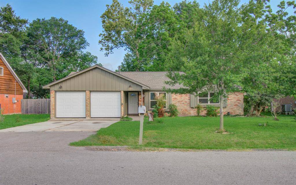 This photo shows a single-story brick house with a two-car garage, a well-maintained lawn, and mature trees, offering a charming and inviting exterior.