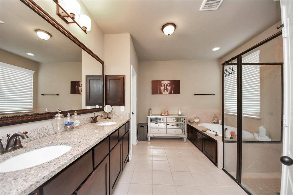 Primary bathroom features a spacious layout with a double sink vanity, large mirror, and granite countertops. It includes a glass-enclosed shower, a separate bathtub, and ample natural light from the windows.